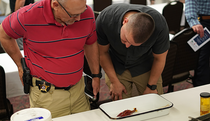 Two men at a table inspect a red crayfish in a container