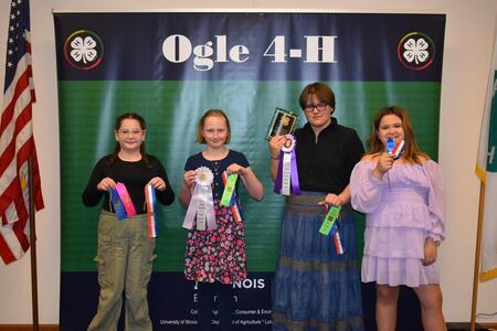 four girls standing in front of Ogle 4-H sign with ribbons