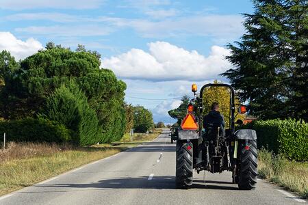 Person driving a tractor without a cab on a rural road.