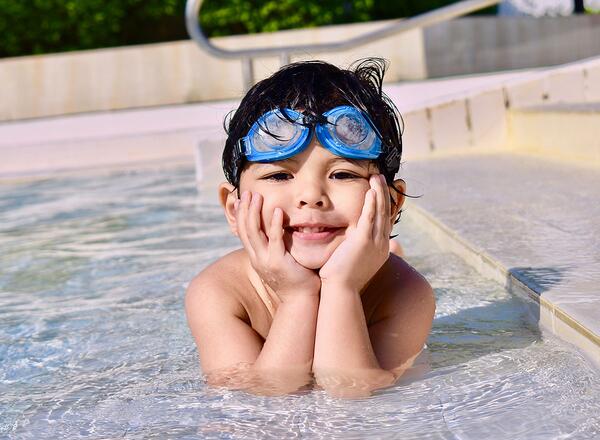 young boy with goggles sitting in pool