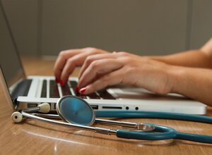 woman typing on computer with stethoscope on desk