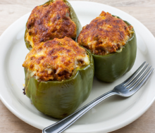 Three stuffed green peppers on a white plate with fork on light tan background