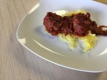 Meatballs and sauce on top of cooked spaghetti squash sitting on a white place on a light wood background