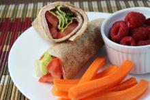 Turkey sandwich wrap on white plate with carrots sticks and raspberries