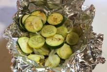 Coin-shaped zucchini and yellow summer squash and sliced white onion on crumpled aluminum foil