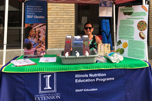 staff member sitting at a booth with nutrition education materials and infused water samples for people visiting a farmers market booth
