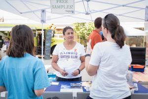 staff member at a farmers market booth answering questions from two community members
