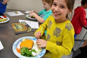 smiling girl in yellow sweater making cheese toast with vegetables on top