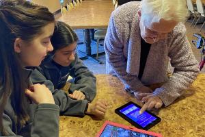 two teen girls teaching an elderly lady about a tablet