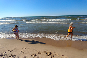 Child carrying beachball walking behind adult on Lake Michigan shore