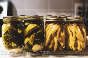 Two jars of canned pickles and two jars of canned wax beans on countertop.