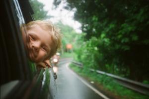 blonde boy puts head out of car window on road