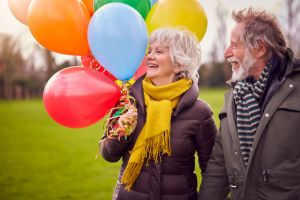 older couple holding large bunch of colorful balloons