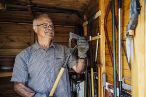 older white male examines garden tool in shed