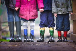 Four young children wearing rain boots and holding hands outside
