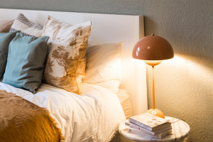 Bed with pillows, sheets, and covers next to a softly lit lamp on nightstand