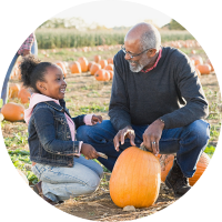 older man and young girl pick out a pumpkin in a field