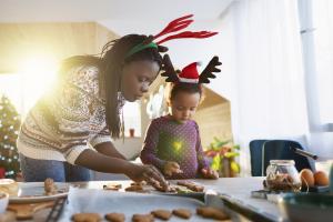 black woman and child in holiday outfits bake cookies