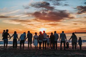 Family and friends of all ages hold hands on beach