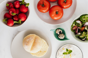 A bowl of tomatoes, strawberries, and cheese along with a plate of english muffins. 