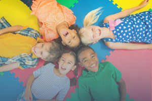 Five smiling kids laying in a circle on a puzzle mat. 