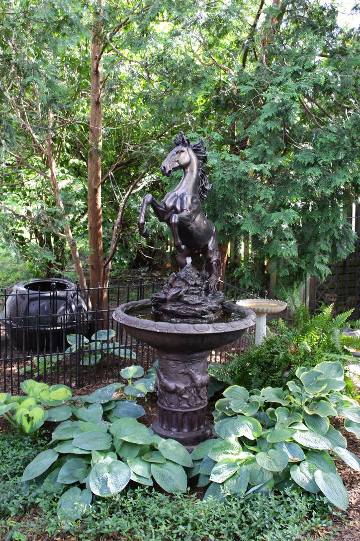 A fountain with a horse standing on its hind legs in a garden.