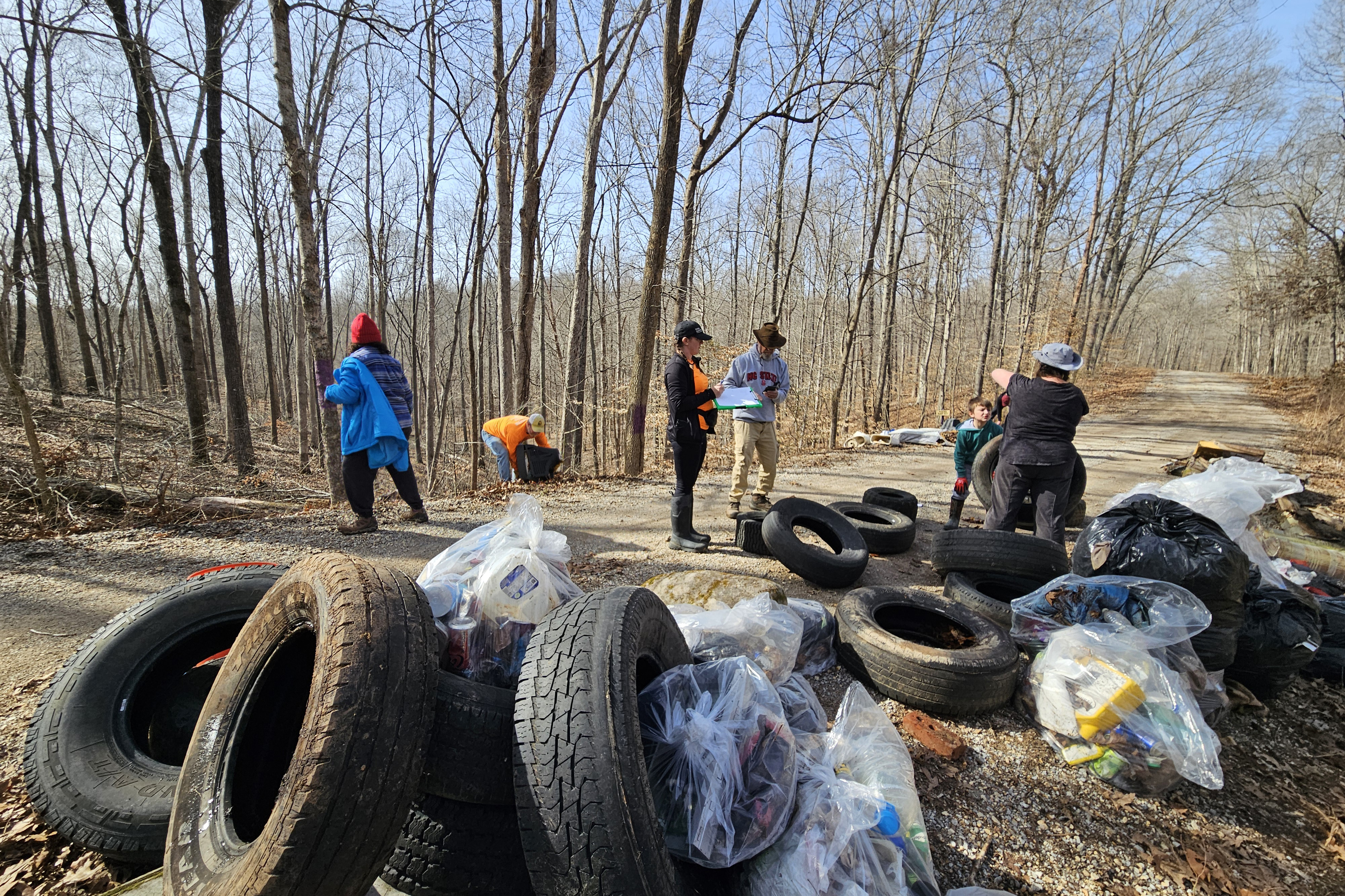 People collect trash from the woods on the side of the road