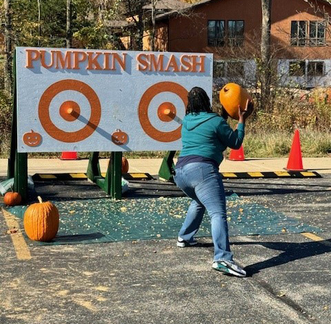 A woman holding a pumpkin throws it at a board