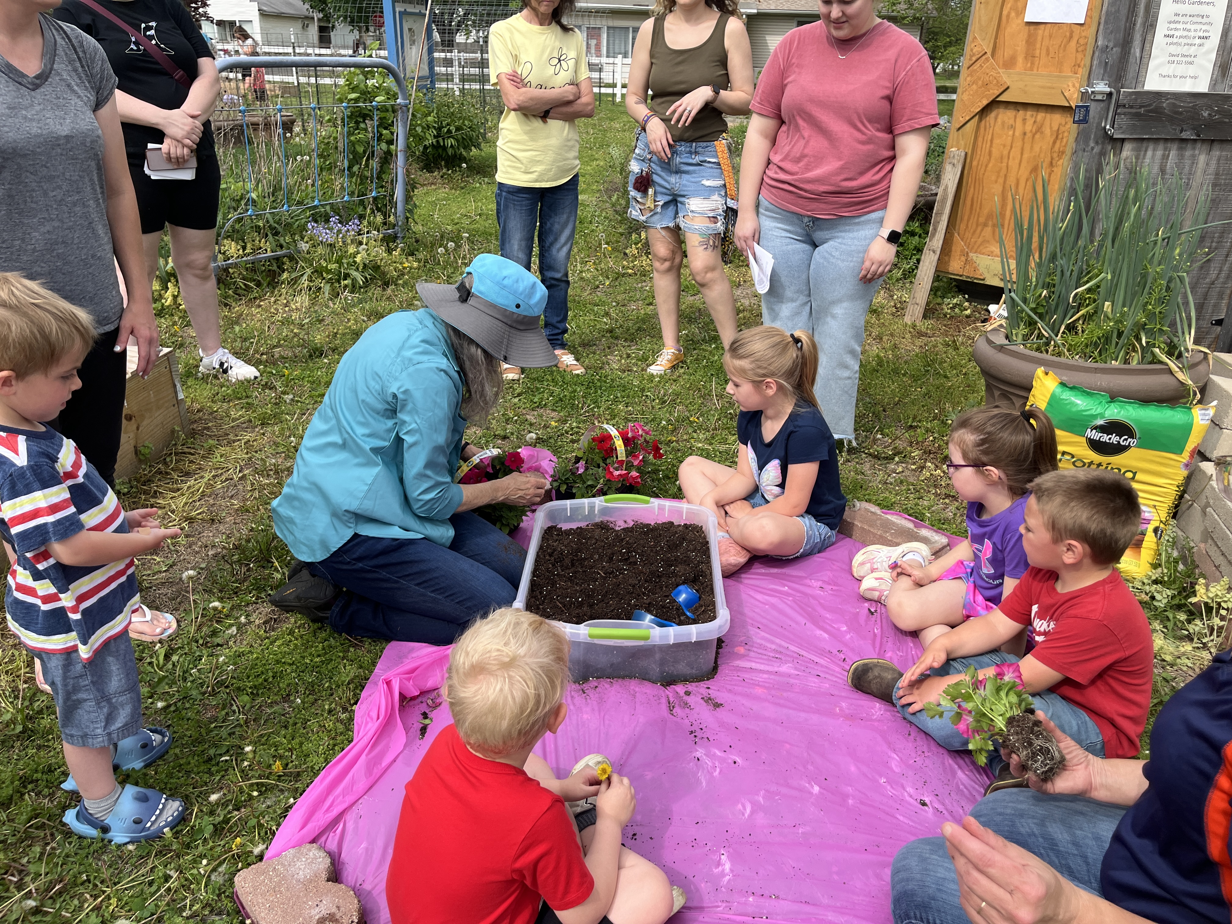 A woman with a container of soil surrounded by children