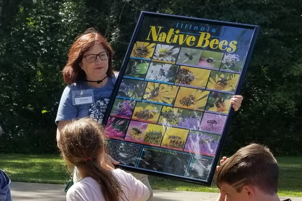 A woman holds a poster for children that says "Illinois native bees"