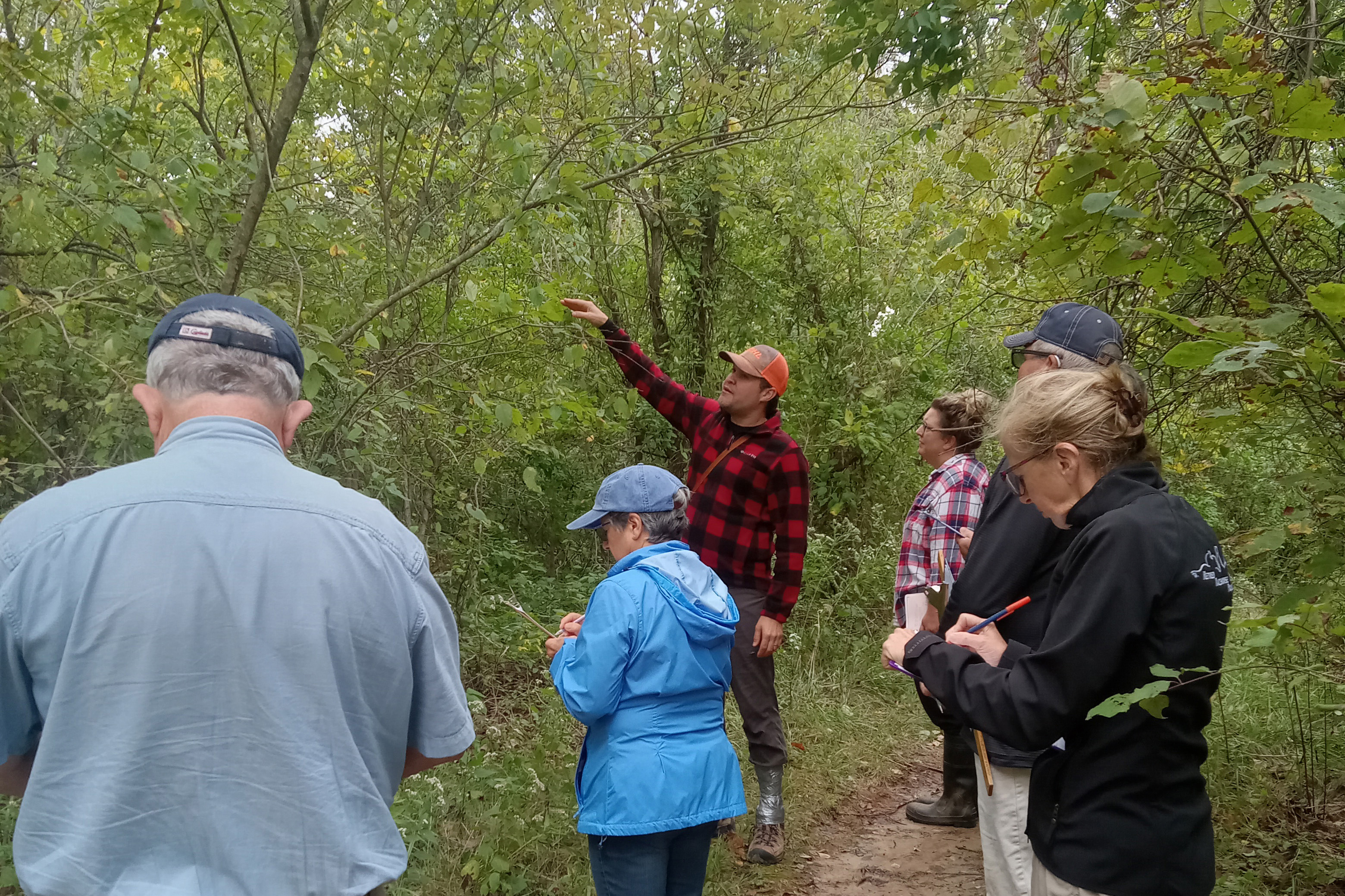 People in the forest taking notes while listening to someone speak
