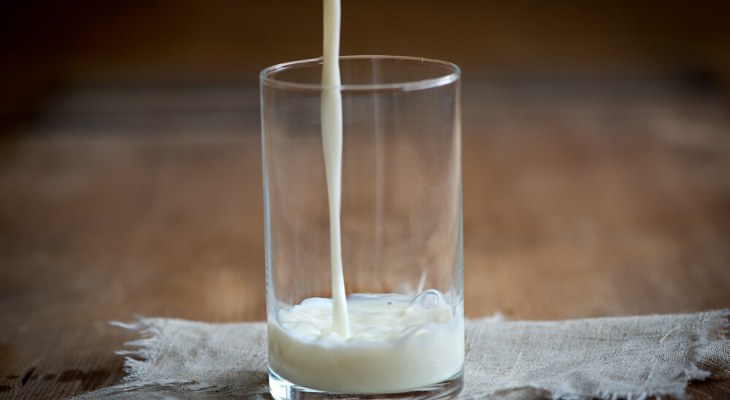 Milk pouring into glass set on wooden table