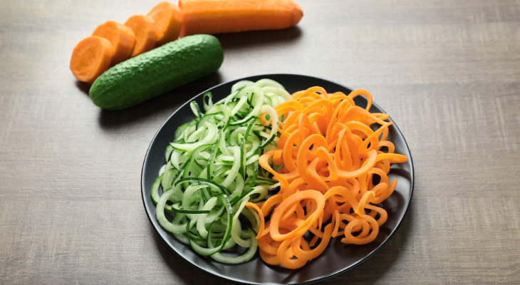Spiralized zucchini and carrot noodles on a black plate, with a whole carrot and zucchini off to the side.
