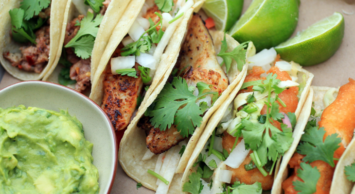 Fish tacos next to limes and a bowl of guacamole