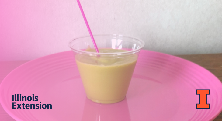 A green smoothie in a clear glass with a pink straw on a pink plate