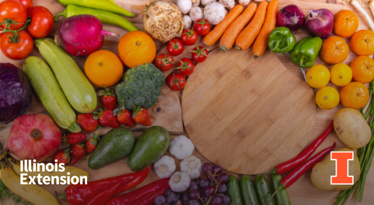 An array of whole fruits and vegetables around a circular wooden cutting board, including carrots, garlic, peppers, tomatoes, oranges, and strawberries. Contains an orange I block logo and Illinois Extension workmark.