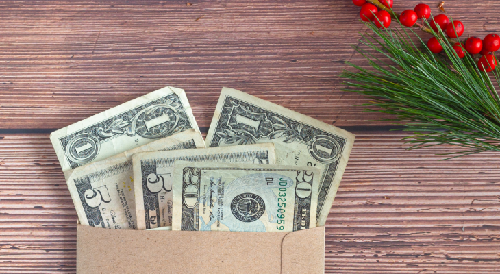 One, five, and twenty dollar bills in an envelope on a table decorated with greenery and red berries.