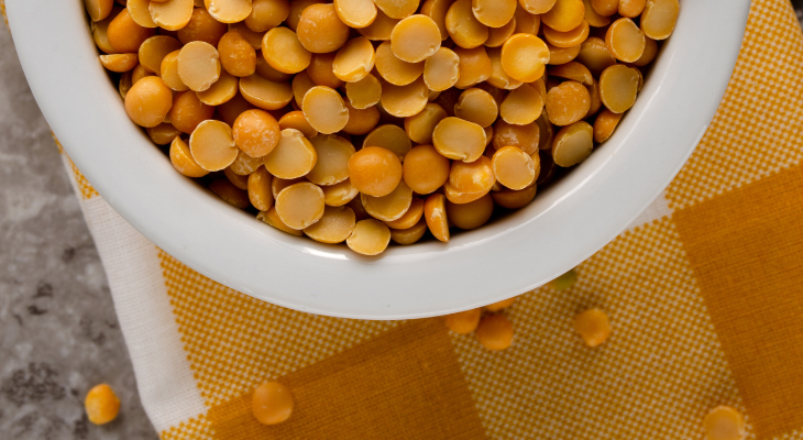 Overhead shot of white bowl of yellow split peas on checkered yellow placemat