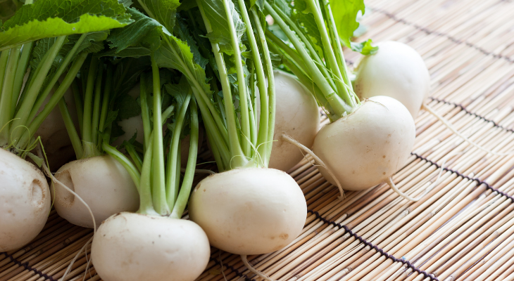 Small white turnips with attached greens on a bamboo mat