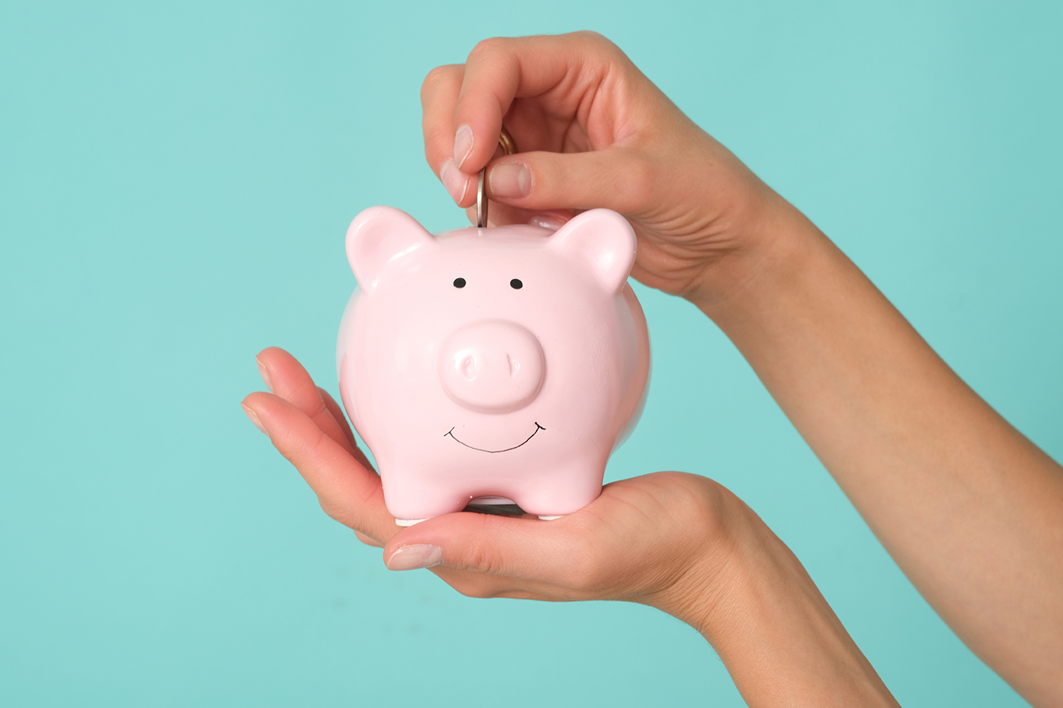 hand putting coins into a pink piggy bank