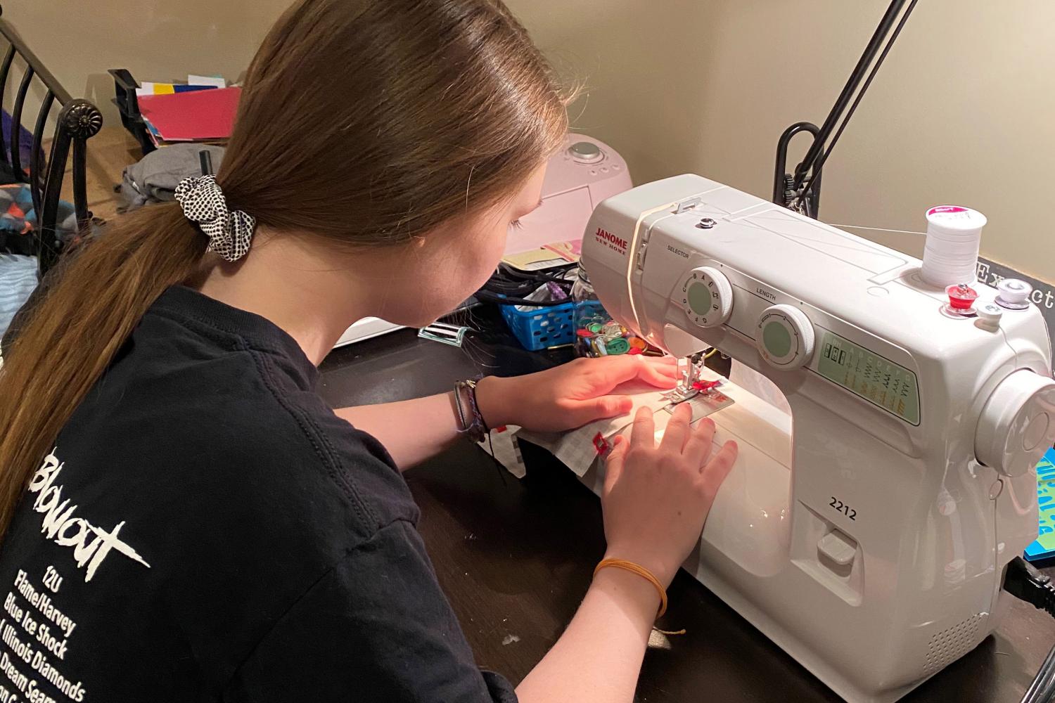 Young woman uses sewing machine to make mask