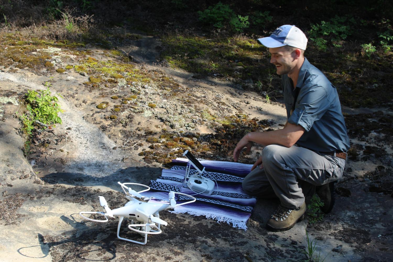 A man crouches next to a drone preparing to take flight
