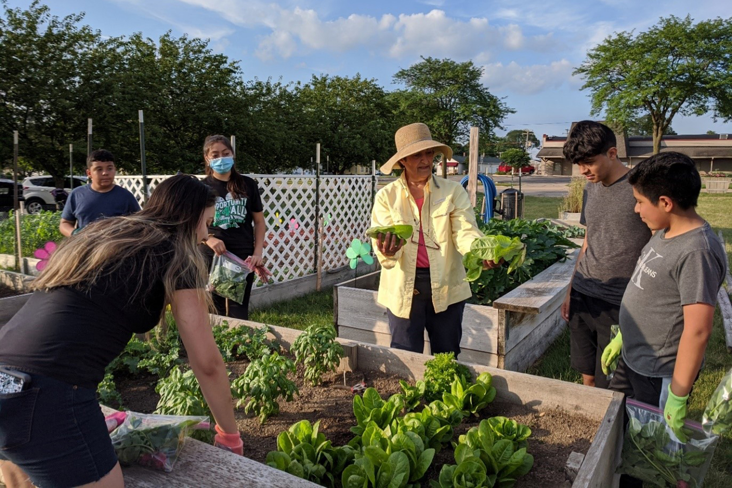 group of children gather around a raised bed garden listening to an older woman holding vegetables