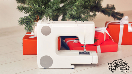 A white sewing machine sitting underneath a tree with presents surrounding the tree.
