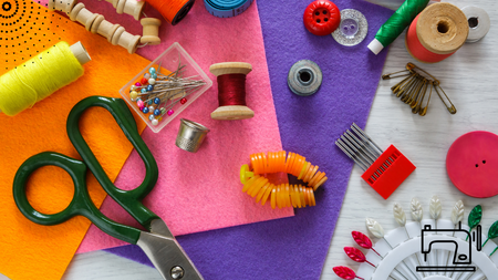 Various sewing accessories - thread, scissor, needles, buttons, thimbles, and pins all laid out on fabric.