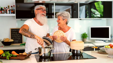 Older couple laughing in the kitchen while cooking food