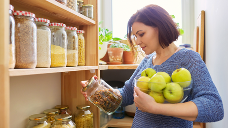 Woman looking in pantry holding jar of food and fruit