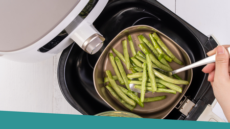 A person using a spoon to take cooked green beans out of the air fryer.