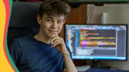 teenager in front of computer with colorful coding showing on screen