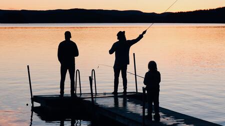 Family fishing off of dock on lake when sun is going down